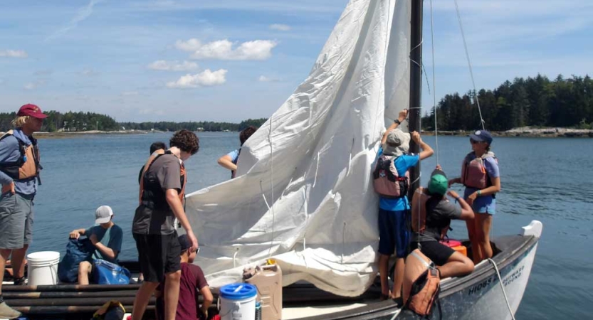 A group of students wearing life jackets adjust the sails of a boat. 